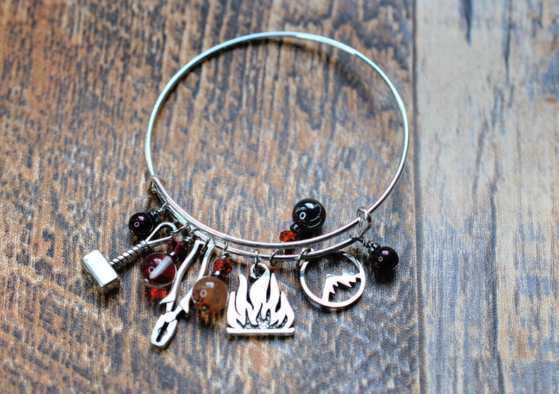 May include: A silver charm bracelet with multiple charms, including a flame, a mountain, a hammer, and a few red and black beads.