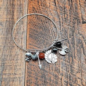 May include: Silver-tone charm bracelet with various pendants, including a skull, arrow, and a warrior's helmet. The bracelet also features red and gray beads and black beads.