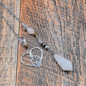 May include: Two silver-toned pendulums with chains and beads. One features a heart-shaped charm with a flame design, the other a faceted rose quartz crystal. The chains have pink and clear beads.