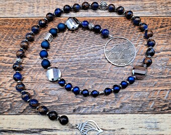 May include: A blue and brown beaded necklace with a silver seashell charm and a silver circle charm with a wave design.