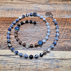 May include: A blue and white prayer bead mala with a silver charm. The mala is made of natural stones and features a variety of blue and white beads.