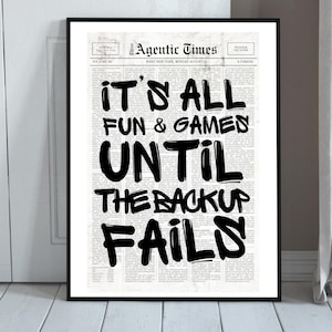 May include: A framed poster featuring a newspaper-style layout titled The Agentic Times. The text reads IT'S ALL FUN & GAMES UNTIL THE BACKUP FAILS in large, bold, black brush-style lettering over a background of small, grey, printed columns.