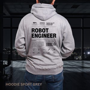 Może przedstawiać: Szara bluza z kapturem z napisem "ROBOT ENGINEER" z tyłu. Bluza ma kaptur ze sznurkiem i kieszeń typu kangur. Tekst "HOODIE SPORT GREY" jest wydrukowany na dole.