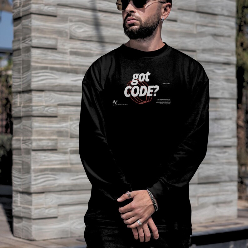 Model wearing a black colored Gildan G18000 crewneck sweatshirt with a retro-tech graphic design featuring the phrase GOT CODE? in bold typography over red orbital linework with small technical details and humorous token-themed microtext.
