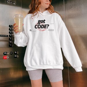 Model wearing a white colored Gildan G18500 pullover hoodie with a retro-tech graphic design featuring the phrase GOT CODE? in bold typography over red orbital linework with small technical details and humorous token-themed microtext.