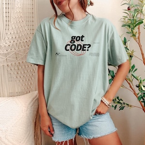 Model wearing a bay Comfort Colors 1717 T-shirt with a retro-tech GOT CODE? graphic featuring bold black typography, red orbital linework, and small technical details.