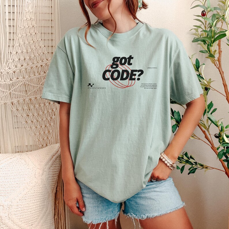 Model wearing a bay Comfort Colors 1717 T-shirt with a retro-tech GOT CODE? graphic featuring bold black typography, red orbital linework, and small technical details.