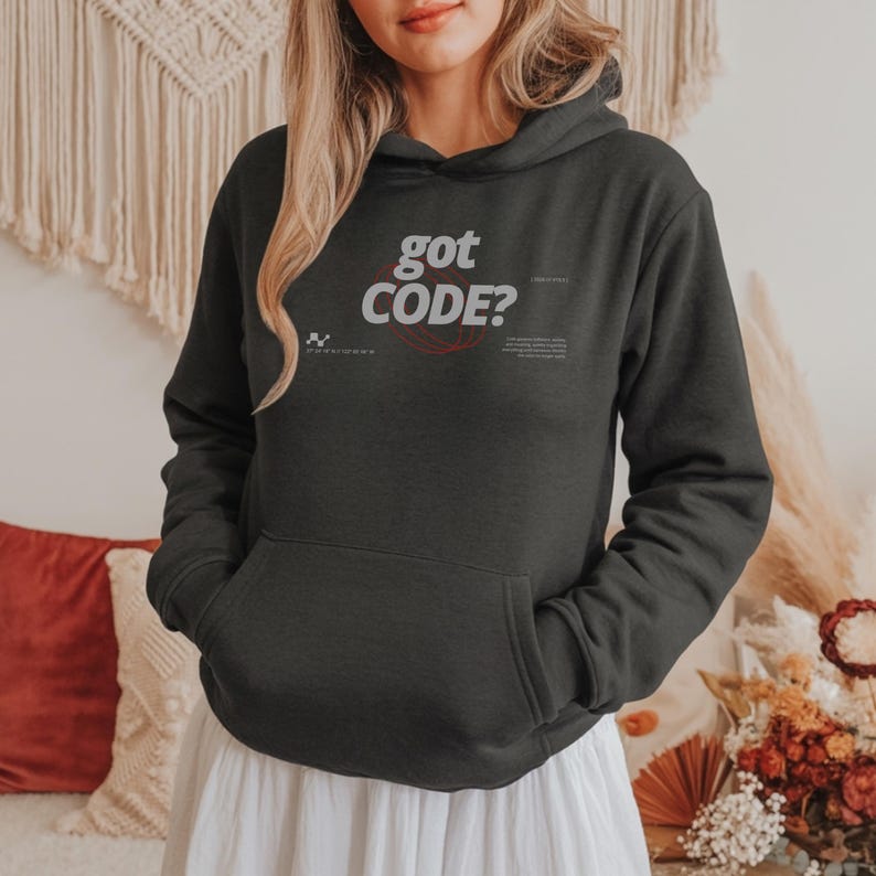 Model wearing a dark heather colored Gildan G18500 pullover hoodie with a retro-tech graphic design featuring the phrase GOT CODE? in bold typography over red orbital linework with small technical details and humorous token-themed microtext.