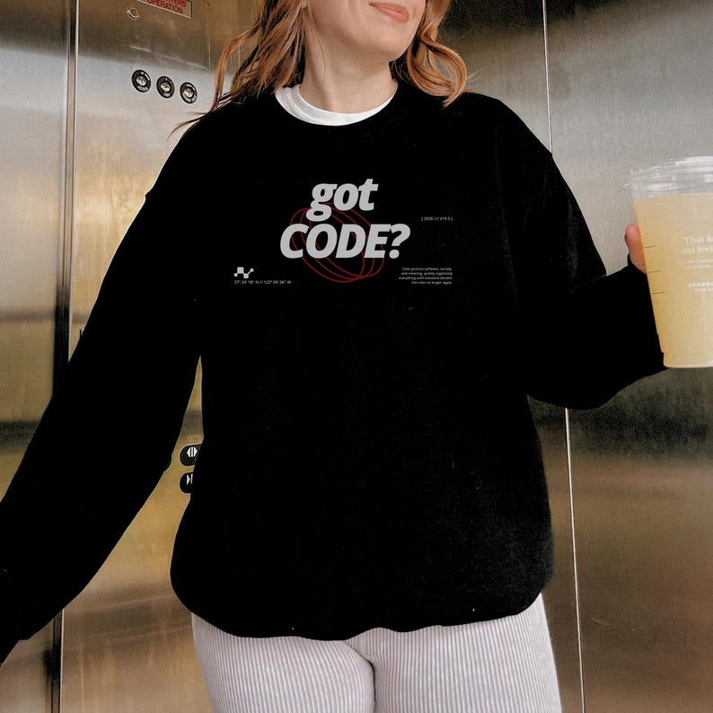 Model wearing a black colored Gildan G18000 crewneck sweatshirt with a retro-tech graphic design featuring the phrase GOT CODE? in bold typography over red orbital linework with small technical details and humorous token-themed microtext.