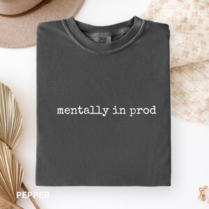 Może przedstawiać: Ciemnoszary t-shirt z okrągłym dekoltem i białym napisem "mentally in prod" nadrukowanym na środku klatki piersiowej. Odzież posiada prążkowany kołnierzyk i standardowy kr&oacute;j, z widoczną metką marki Comfort Colors wewnątrz dekoltu.