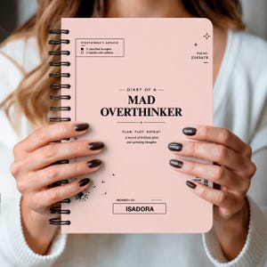 May include: A light pink spiral-bound notebook with black text that reads DIARY OF A MAD OVERTHINKER, PLAN. PLOT. REPEAT., and PROPERTY OF: ISADORA. The cover features graphic details including a file number, checkboxes, and a small dandelion illustration.