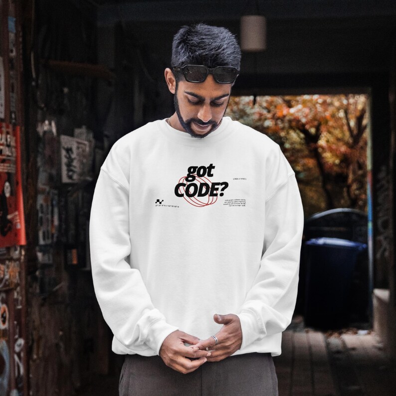 Model wearing a white colored Gildan G18000 crewneck sweatshirt with a retro-tech graphic design featuring the phrase GOT CODE? in bold typography over red orbital linework with small technical details and humorous token-themed microtext.