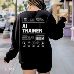 Puede incluir: Una sudadera negra con el texto "AI TRAINER" en letras blancas. La parte posterior de la sudadera presenta texto y elementos gráficos adicionales, incluidas las palabras "EXPERTISE" e "INGREDIENTS". La palabra "BLACK" está impresa en la parte inferior.