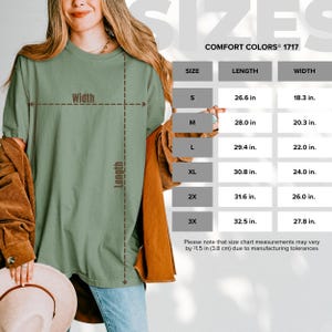 Może przedstawiać: T-shirt w kolorze szałwiowej zieleni z nałożoną tabelą rozmiar&oacute;w Comfort Colors 1717. Tabela zawiera rozmiary od S do 3X z wymiarami długości i szerokości w calach, uwzględniając możliwą tolerancję produkcyjną wynoszącą 3,8 cm.
