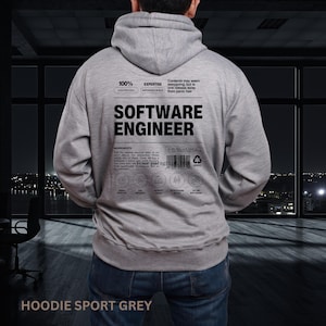 May include: A light grey hooded sweatshirt featuring black text on the back. The design mimics a nutrition label with the words SOFTWARE ENGINEER in large font, along with smaller text, a barcode, and five circular icons at the bottom.