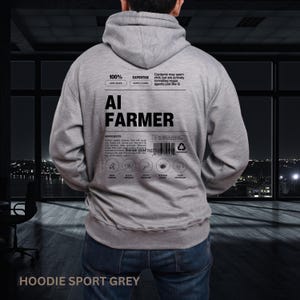 Pode incluir: Um moletom cinza com o texto "AI FARMER" nas costas. Texto adicional inclui "100% HERO MODE", "EXPERTISE SUPPLY CHAIN" e uma lista de ingredientes. O moletom é rotulado como "HOODIE SPORT GREY".
