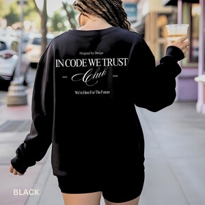 Puede incluir: Sudadera negra con texto blanco. El texto en la parte posterior dice "IN CODE WE TRUST Club" con los años 1843 y 2026. El texto "Original by Design" y "We're Here For The Future" también están impresos. La palabra "BLACK" está impresa en la parte inferior.