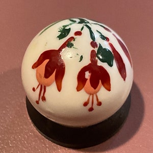 Può includere: Un marmo di ceramica bianca con fiori rossi e rosa e foglie verdi dipinti a mano. Il marmo è su una base nera.