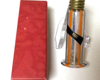Könnte beinhalten: Eine Vintage-Parfümflasche mit goldenem Deckel und einem transparenten Glaskörper mit vertikalen Streifen in Orange, Blau und Weiß. Die Flasche wird von einem transparenten Kunststoffständer gehalten, und das Etikett lautet "ROSE". Eine rote rechteckige Schachtel befindet sich neben der Flasche.