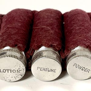 Può includere: Tre piccoli contenitori rotondi in metallo argentato con rivestimenti in feltro rosso. I contenitori sono etichettati "LOTION", "PROFUMO" e "POLVERE".