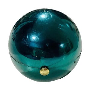 Op de afbeelding: Een teal-kleurig, bolvormig object met een glanzend, reflecterend oppervlak. De bol heeft een naad rondom en een kleine, goudkleurige knop aan de onderkant. Het object lijkt een decoratief item of een container te zijn.
