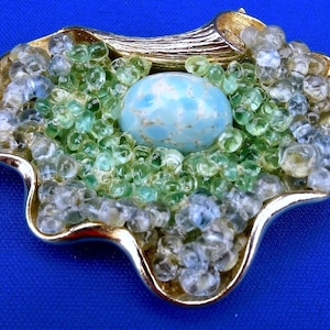 May include: A gold-tone brooch featuring a blue and white cabochon stone set amongst green and clear glass beads.