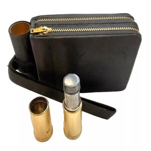 May include: Black leather fanny pack with two zippered compartments and a gold zipper. Includes a matching black strap and a cylindrical holder. Two gold-colored bullet-shaped containers are also present, one with a glass vial inside.