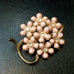 Puede incluir: Un broche de tono dorado con un grupo de flores de esmalte rosa con centros de diamantes de imitación transparentes. Las flores están dispuestas en un tallo de tono dorado.