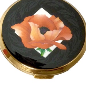 Può includere: Un compatto dorato con sfondo in smalto nero e un fiore di papavero arancione dipinto a mano in una forma di diamante bianco.