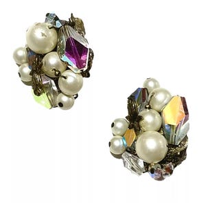 May include: Two vintage clip-on earrings. Each earring features a cluster of faux pearls, iridescent crystals, and metallic accents. The pearls are various sizes, and the crystals have a faceted, geometric shape. The earrings have a classic, elegant design.