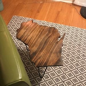 May include: A wooden table shaped like the state of Wisconsin, with a dark brown stain. The table has black hairpin legs and is sitting on a white and brown patterned rug.
