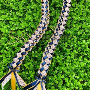 May include: A white, blue, and gold baseball-themed lei with the numbers 2024 and #6 on it. The lei is made of ribbon and has a bow at each end.