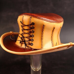 May include: A tan leather top hat with a brown leather brim and a brown leather lace-up detail.
