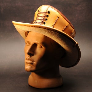 May include: A tan leather hat with a tall, pointed crown and a wide brim. The crown has a lace-up detail and the brim is stitched with brown thread.
