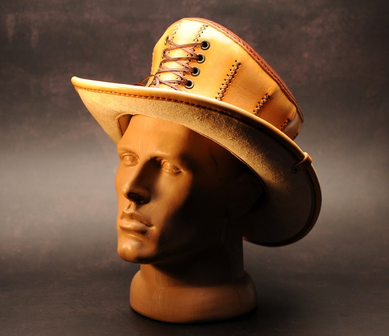 May include: A tan leather hat with a tall, pointed crown and a wide brim. The crown has a lace-up detail and the brim is stitched with brown thread.
