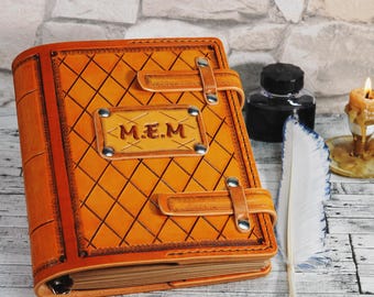 Può includere: Un diario rilegato in pelle marrone con un motivo a rombi e le iniziali "M.E.M." in rilievo sulla copertina. Il diario è chiuso e ha un raccoglitore ad anelli.