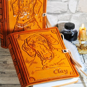 May include: Two leather-bound journals with embossed dog portraits. The journal on the right has the name "Clay" embossed on the cover.