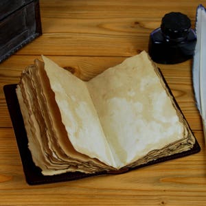 May include: An open, antique-style journal with blank pages, a vintage inkwell, and a white feather quill pen on a wooden table.