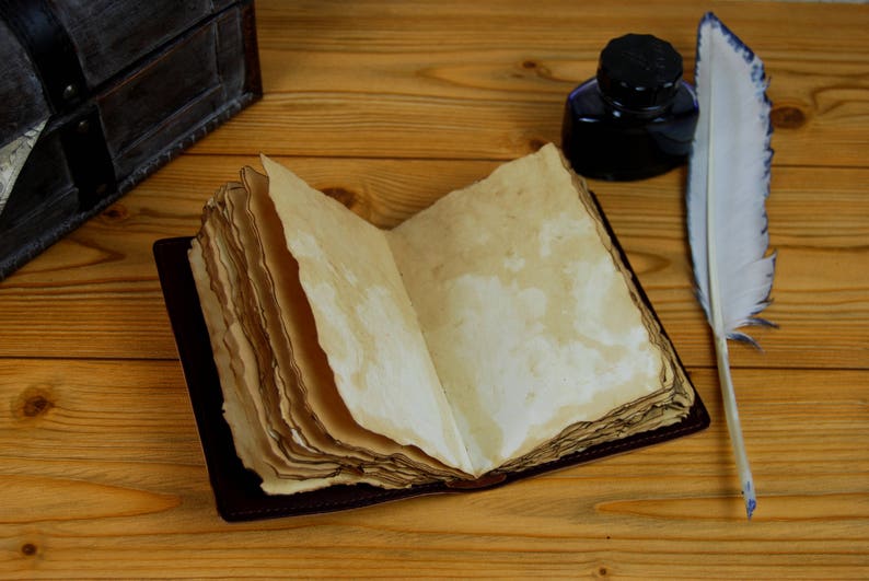 May include: An open, antique-style journal with blank pages, a vintage inkwell, and a white feather quill pen on a wooden table.