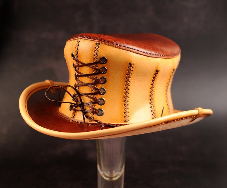 May include: A tan leather top hat with a brown leather brim and a brown leather lace-up detail.