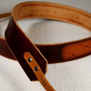 May include: A brown leather camera strap with a tan leather accent and the text "TIVY" embossed on the strap.