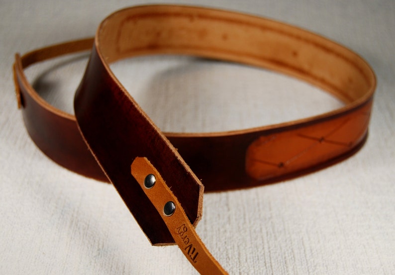 May include: A brown leather camera strap with a tan leather accent and the text "TIVY" embossed on the strap.