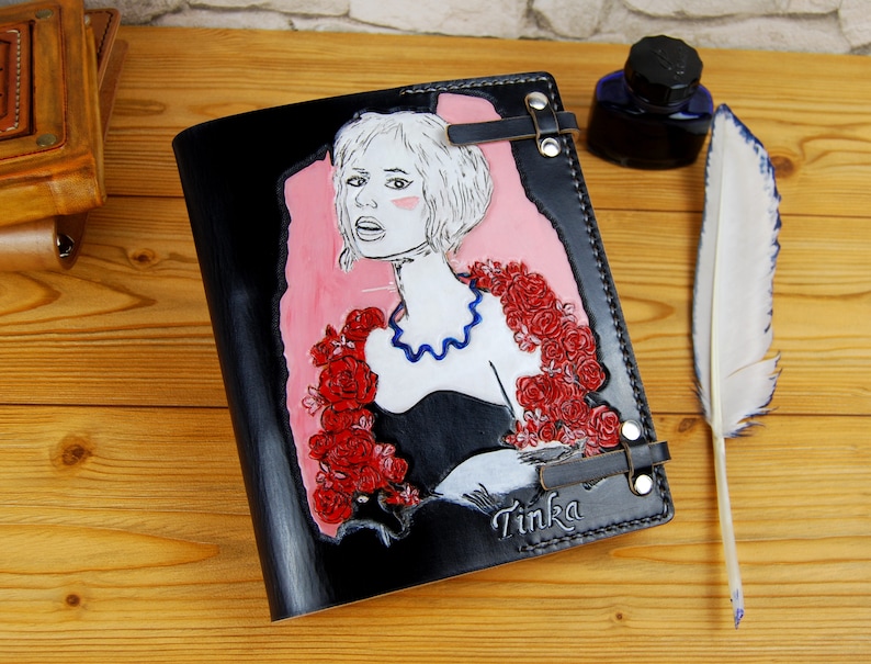 May include: Black leather journal with a portrait of a woman with red roses and the word "Tinka" on the cover.