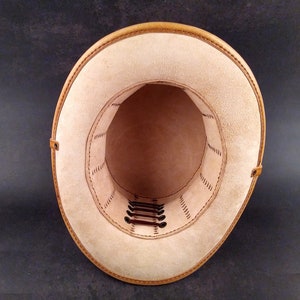 May include: The inside of a tan leather hat with a brown leather band and stitching. The hat has a series of brown leather laces that are threaded through holes around the crown.