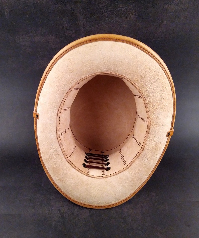May include: The inside of a tan leather hat with a brown leather band and stitching. The hat has a series of brown leather laces that are threaded through holes around the crown.