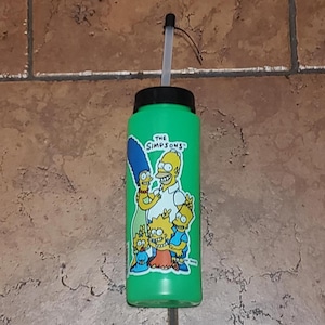 May include: Green water bottle with a straw and a sticker featuring the Simpsons family. The sticker says "The Simpsons".