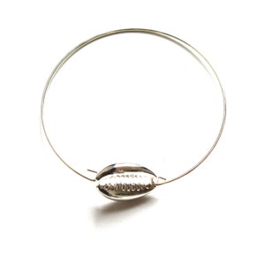 May include: A silver bangle bracelet with a shell charm. The shell is detailed with a textured pattern.