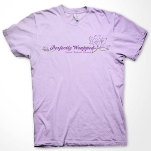 May include: A lavender t-shirt with the text "Perfectly Wrapped" and a purple flower graphic. The text below the graphic reads "Revived, Restored, Released."