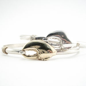 May include: Two silver bracelets with gold lobster claw charms. The bracelets are stacked on top of each other.