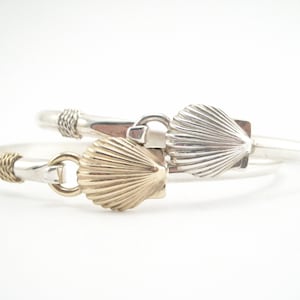 May include: Two silver bracelets with a shell charm. One shell charm is gold and the other is silver.